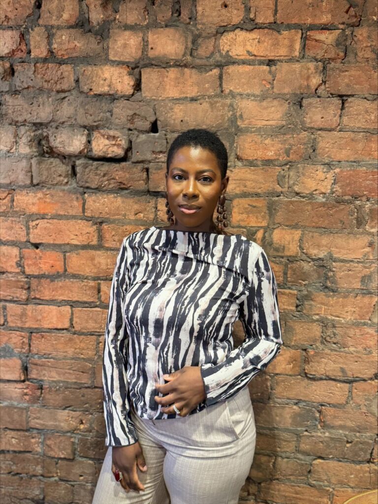 Picture of Beatrice Anomah looking at the camera, standing in front of a brick wall background