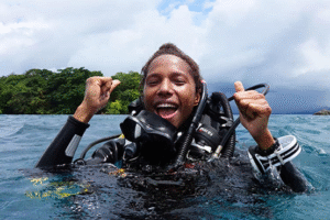 Picture of Naomi Longa smiling and cheering while wearing scuba gear, in the sea in Papua New Guinea